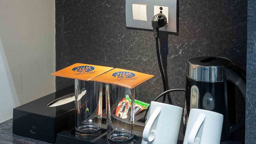 Image of Coral Premium Room at Coral Reef Hotel and Spa in Port Blair showing tea and coffee maker along with cups and glasses and coffee sachets on a tray above which a golden showpiece is placed on the shelf