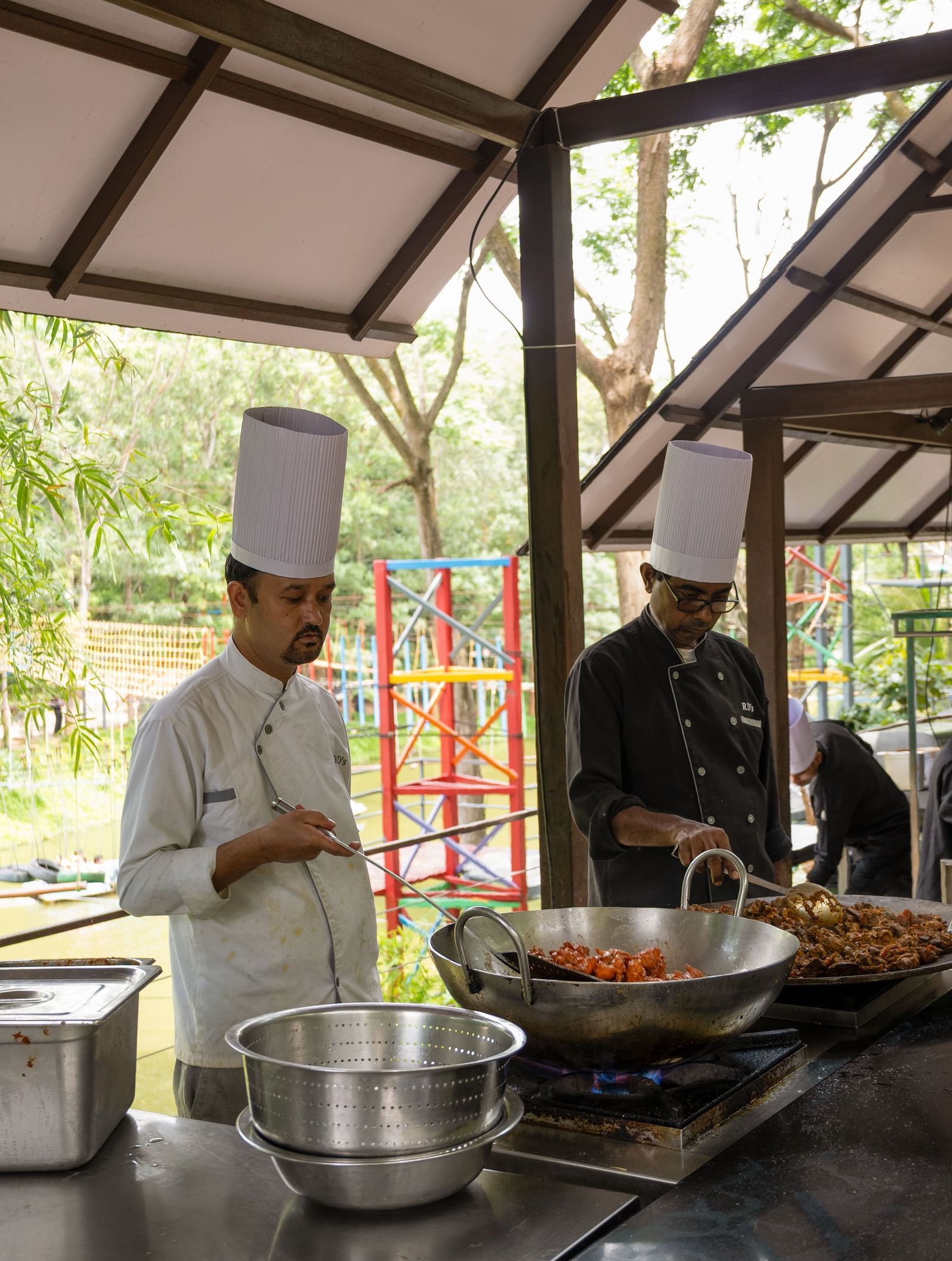 A chef stands in a professional kitchen preparing food at a wok station under a high, open-air roof structure | Lake View Restaurant
