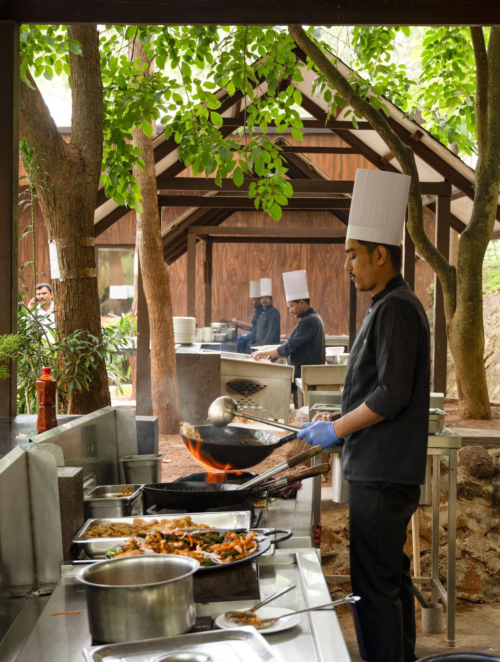 A chef in a white uniform prepares food at a buffet station in a dining area surrounded by lush greenery and large windows | Lake View Restaurant