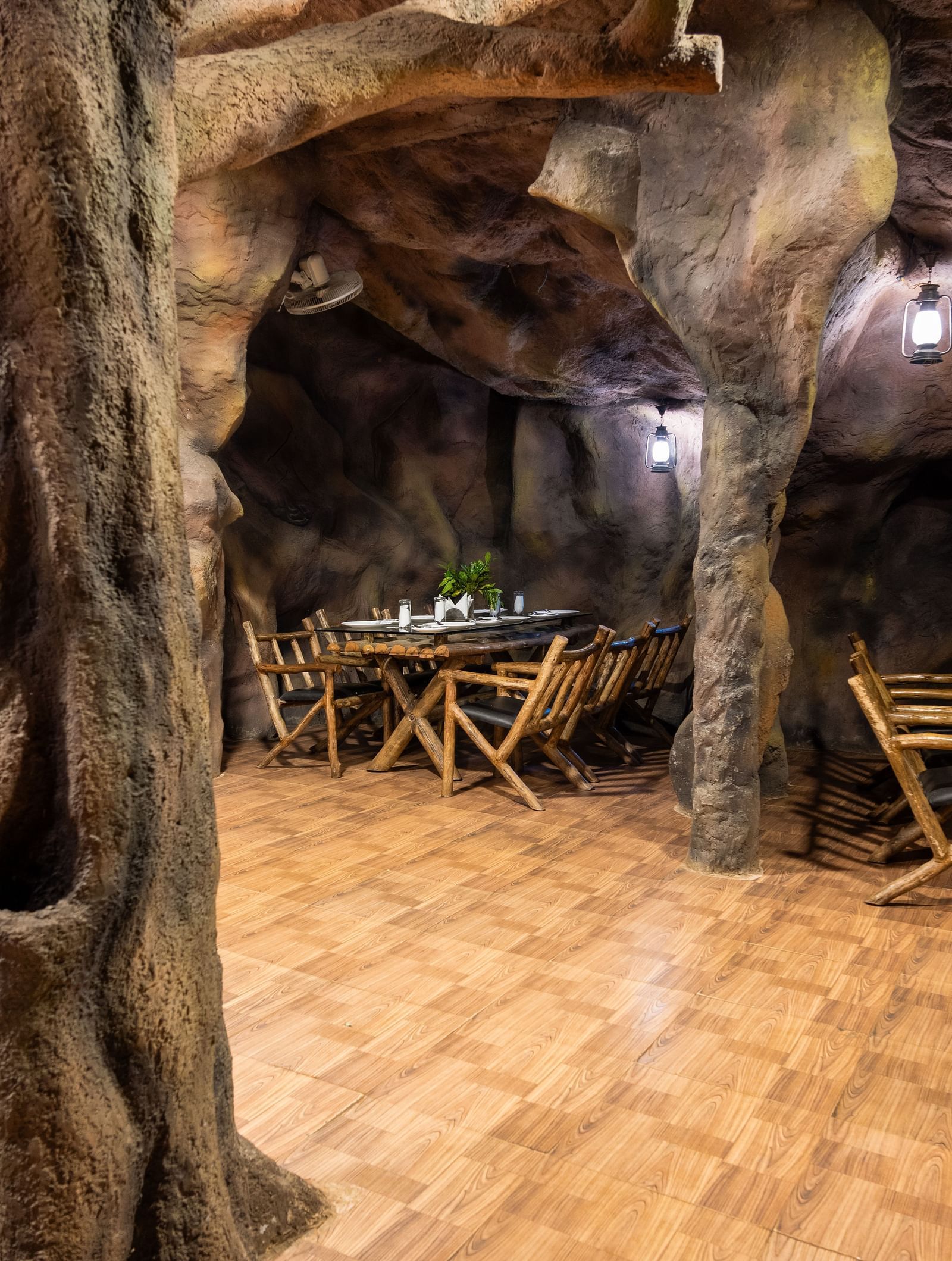 A central area within the cave-themed restaurant highlights a large, artificial tree trunk surrounded by dining tables and chairs under ambient lighting | Cave Restaurant