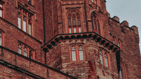 Facade of a historic castle building with red-bricked walls featuring Romanesque revival architecture.