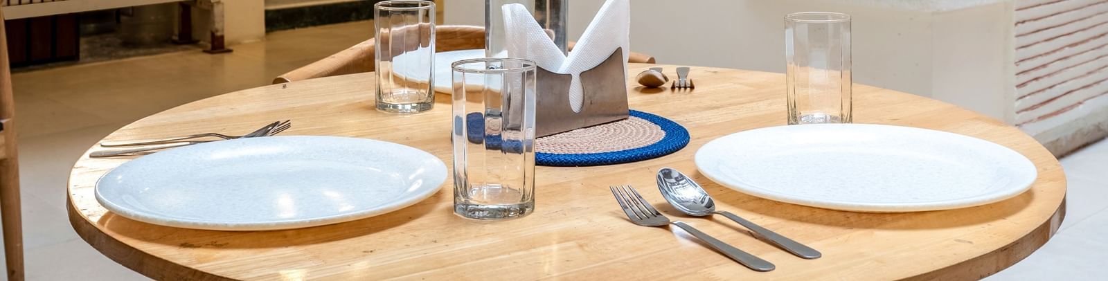 A round dining table set for 2 with plates, glasses, and cutlery - Monday Hotels HITEC City, Hyderabad