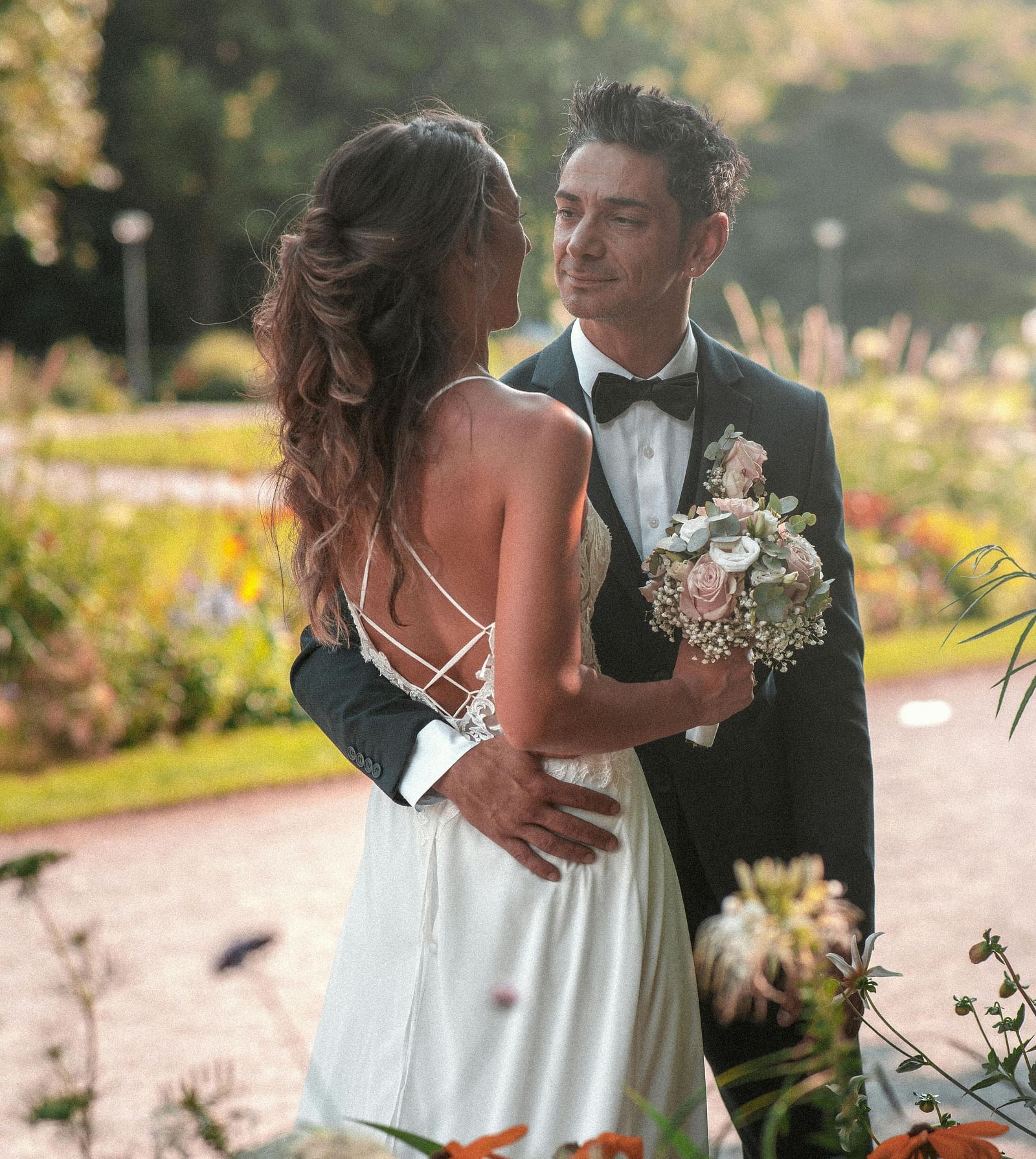 A bride and a groom posing for a photo with flowers in the foreground