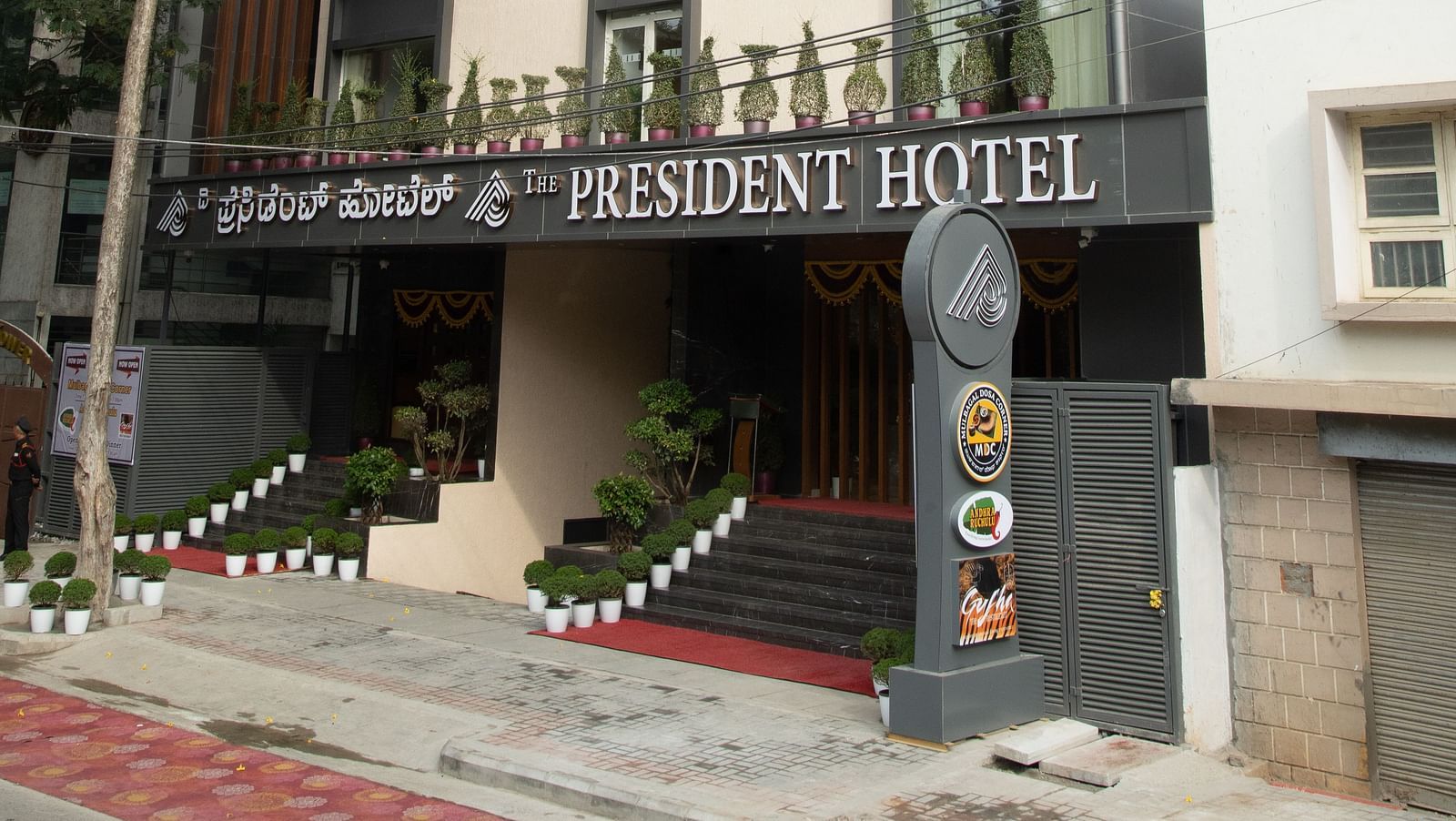 An image of frontal view of a hotel's exterior showcasing its architecture and entrance - The President Hotel, Kumara Park, Bangalore