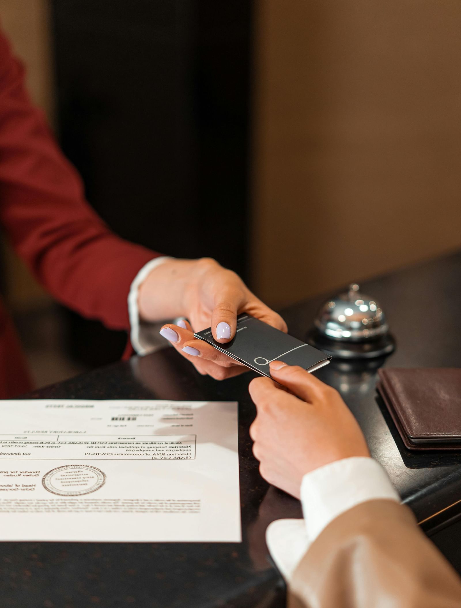 A hotel employee in a red jacket handing a key card to a guest at the reception desk.