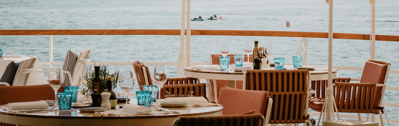 An outdoor dining table set with chairs featuring a distant view of the ocean at Trishvam Palolem Beach Resort, Goa.