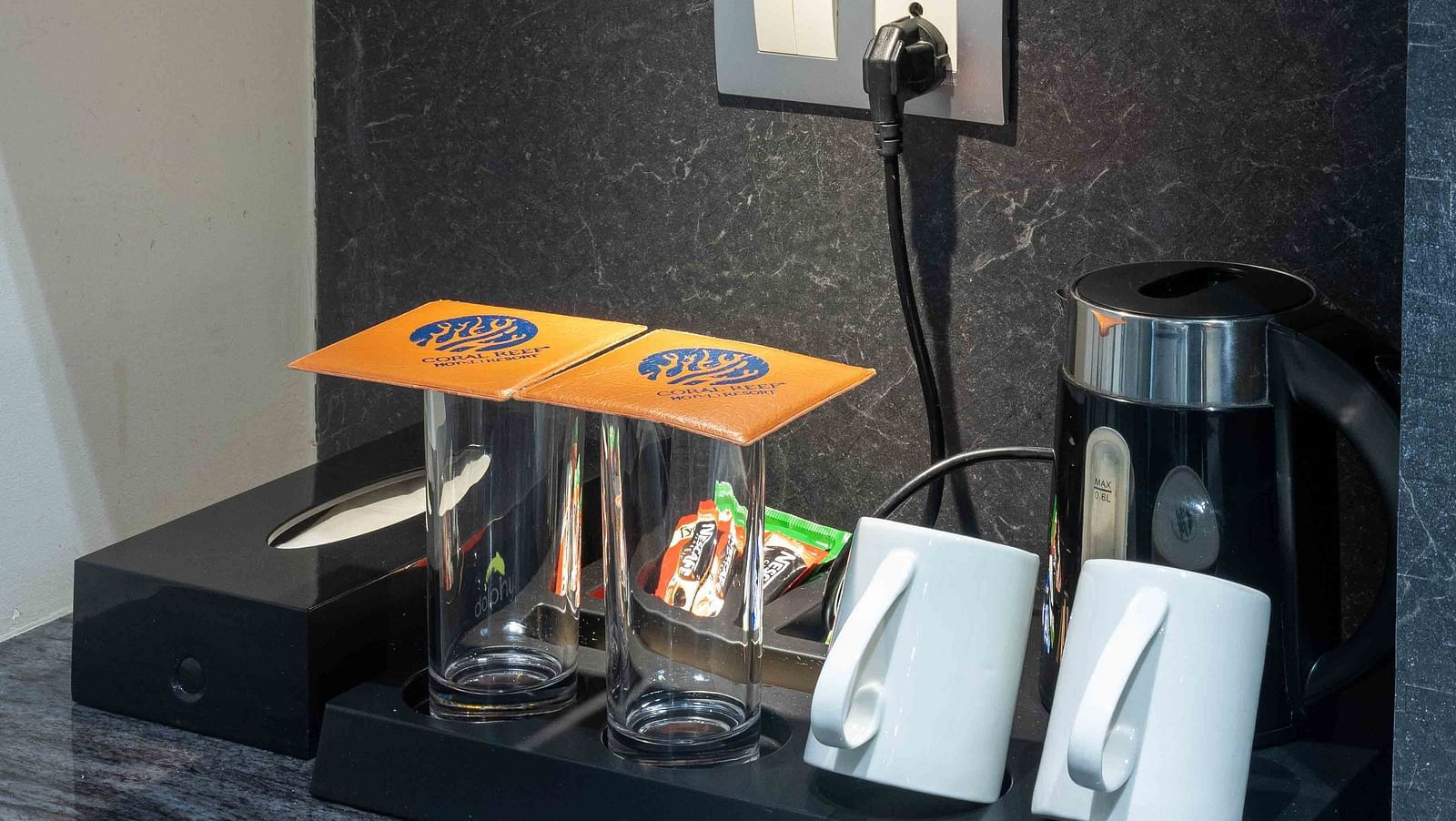 Image of Coral Premium Room at Coral Reef Hotel and Spa in Port Blair showing tea and coffee maker along with cups and glasses and coffee sachets on a tray above which a golden showpiece is placed on the shelf