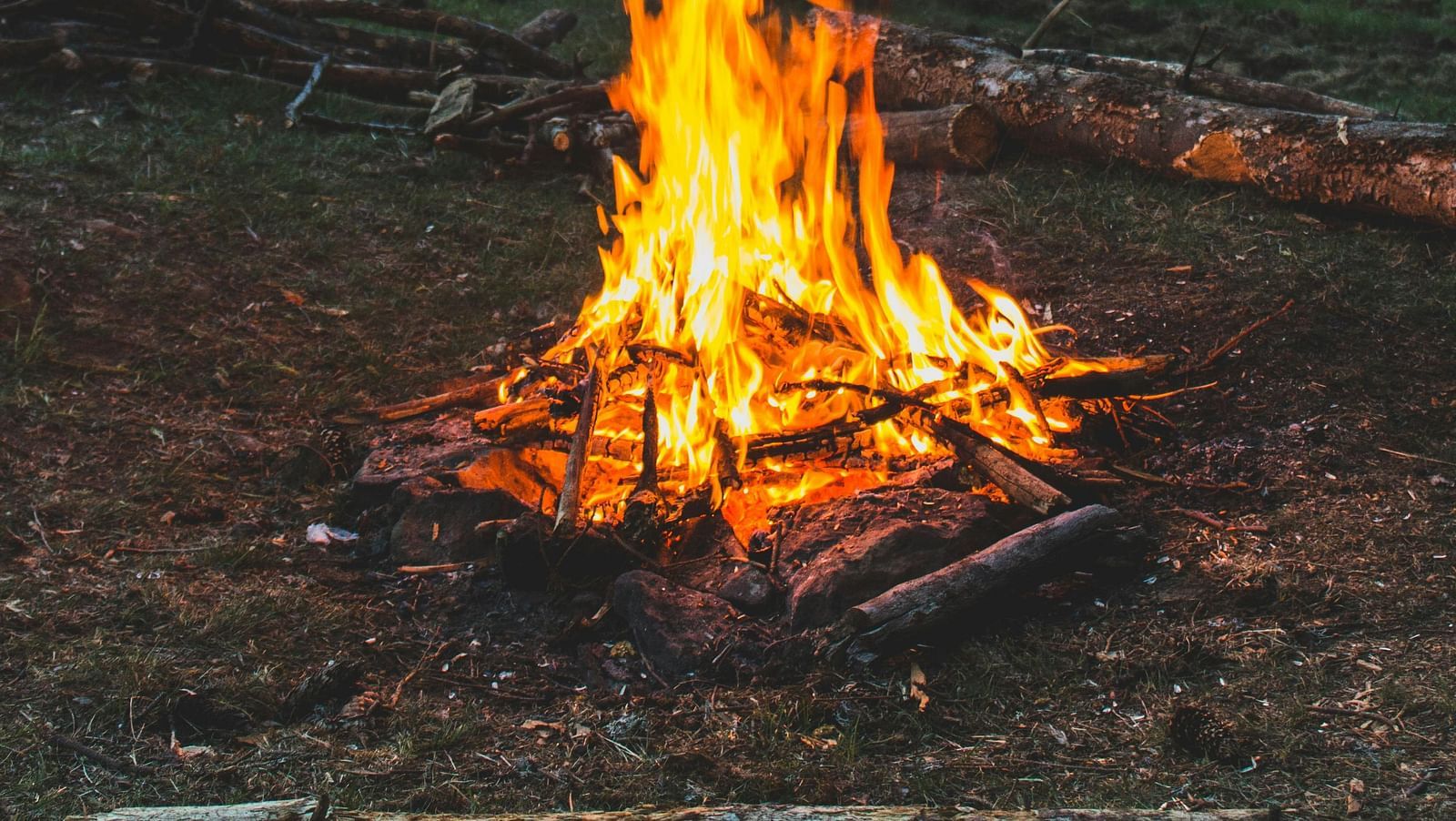 A campfire burns brightly in a mountain landscape at dusk.
