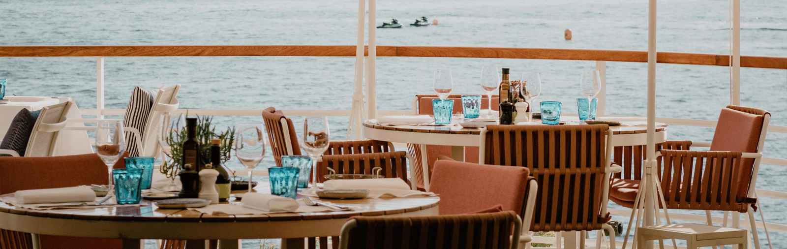 An outdoor dining table set with chairs featuring a distant view of the ocean at Trishvam Palolem Beach Resort, Goa.