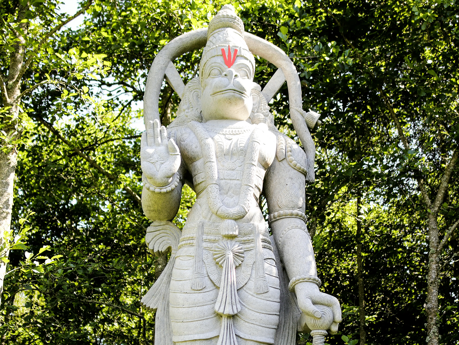A white marble statue of Lord Hanuman standing amidst dense foliage.