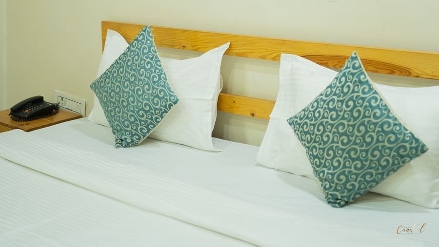 A close-up of a large bed with 2 blue pillows and a framed picture on the wall, at Daksh Resort & Amusement Park, Sasan Gir.