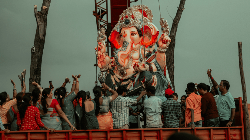 A view from afar of a the Ganesh idol with people surrounding it at Lalbaugcha Raja, with trees behind it.