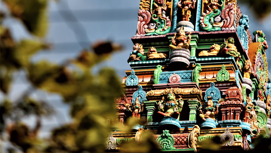 A temple's roof seen in the distance having intricate carvings of deities on them.
