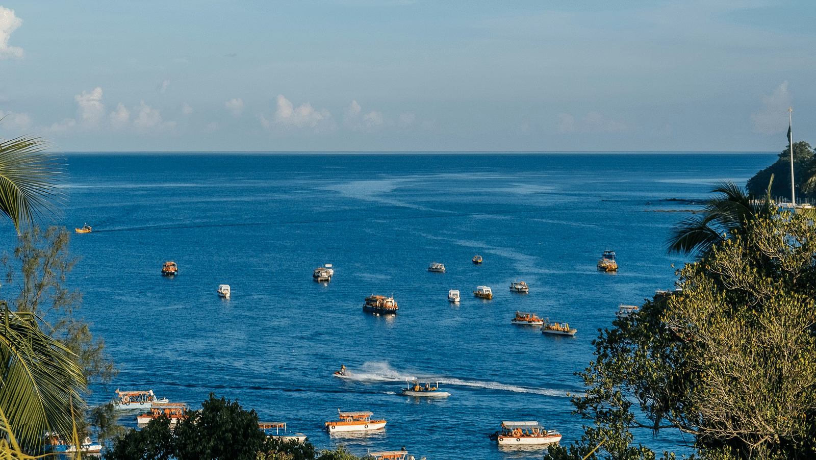 A serene view of a coastal skyline with several boats scattered on the blue water under a clear sky