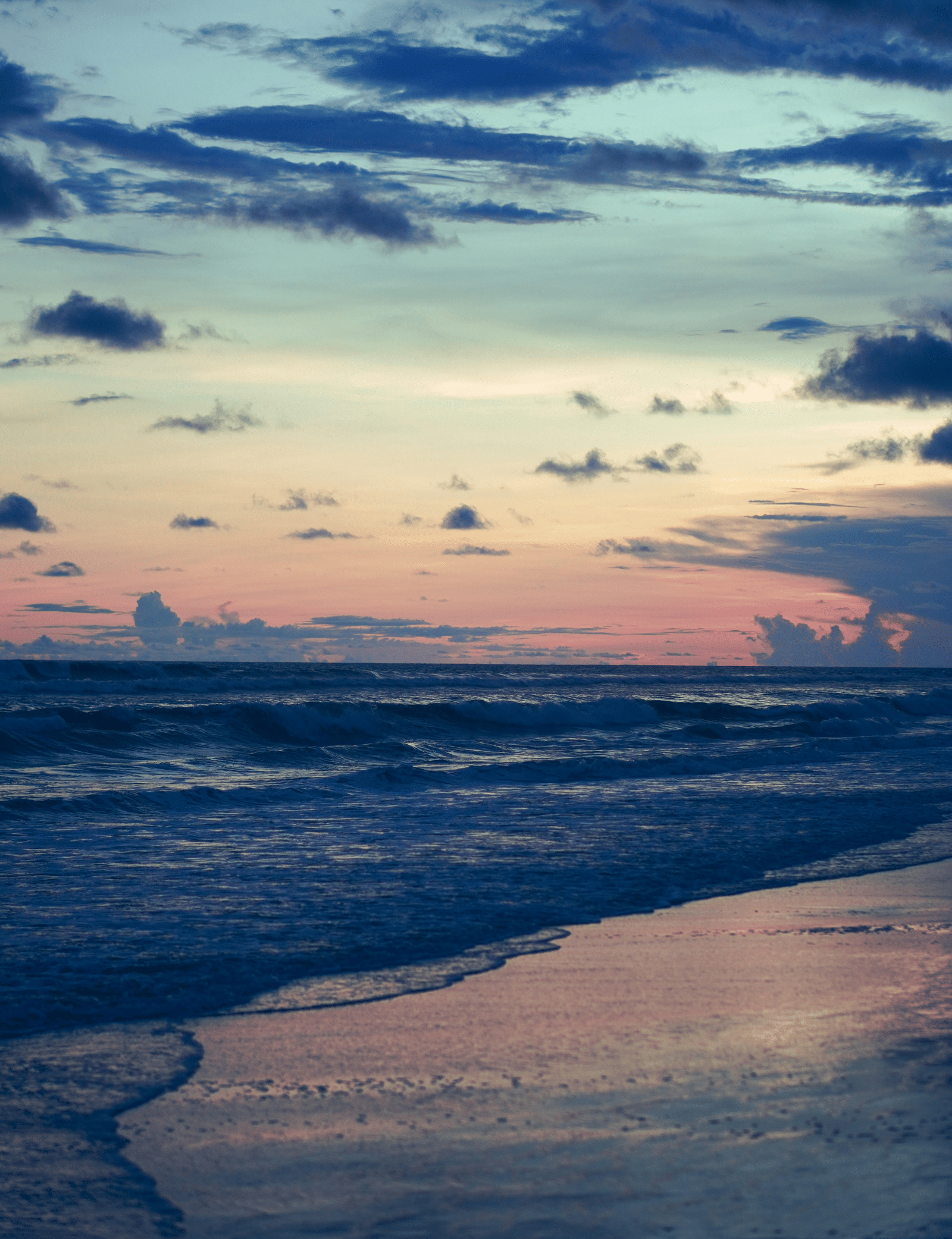Seashore reflecting yellow hue of light under a cloudy sky.