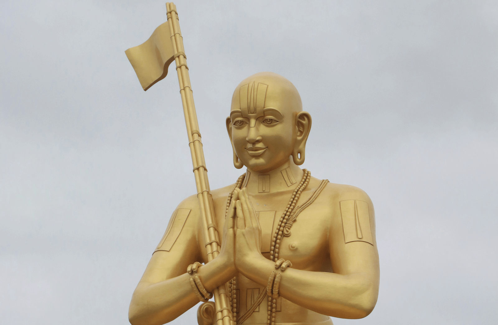 A large golden seated statue holding a flag on a raised plinth against the sky