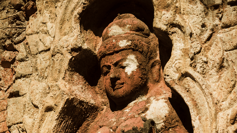 A detailed historical stone relief carving of a traditional female figure embedded in an ancient temple wall.