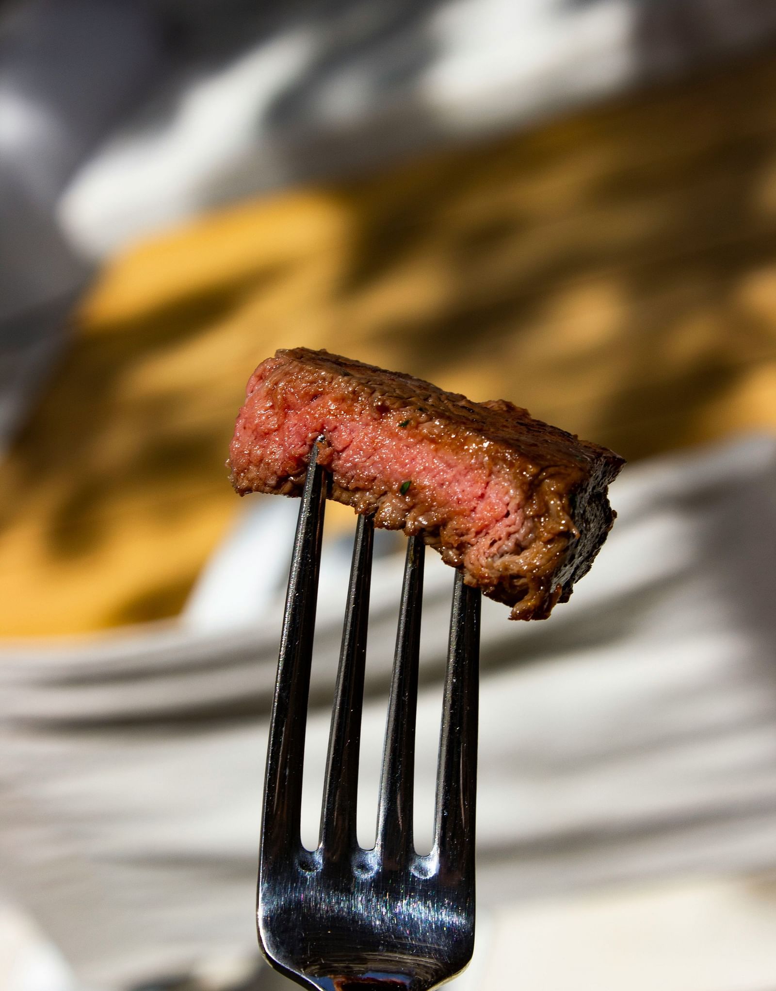 A slice of steak held up by a fork.