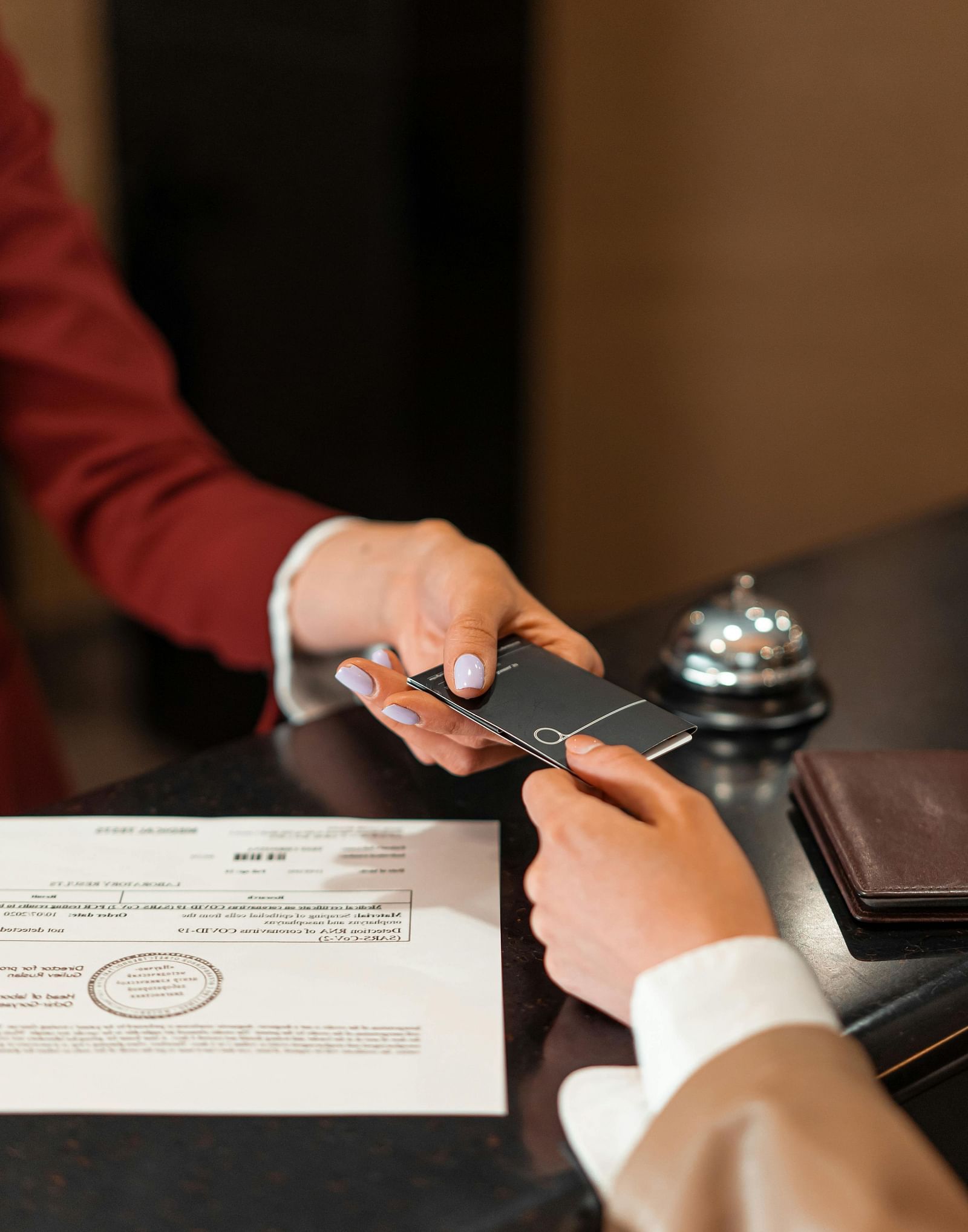 A person behind the reception desk handing over a card to another person with a sheet kept over the desk.