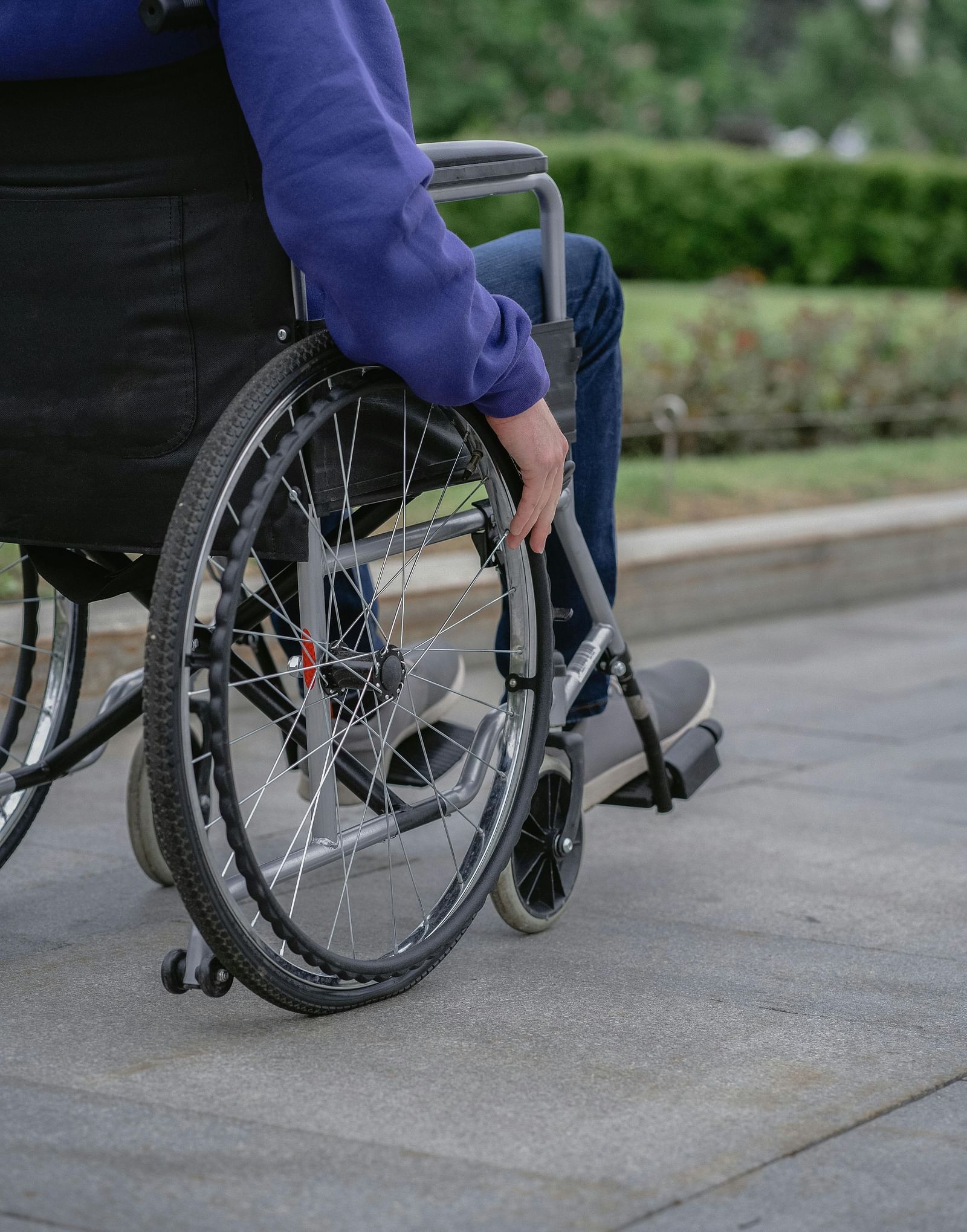 Close up shot of a person sitting on a wheelchair with his hand on the wheel.