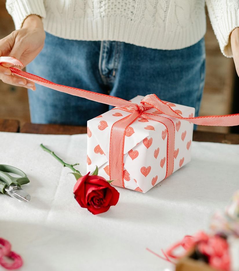 An image of a woman unwrapping a gift box from galentines day and there is also a rose lying next to it