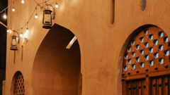Two men in traditional white attire walking through a warmly lit alley at night.