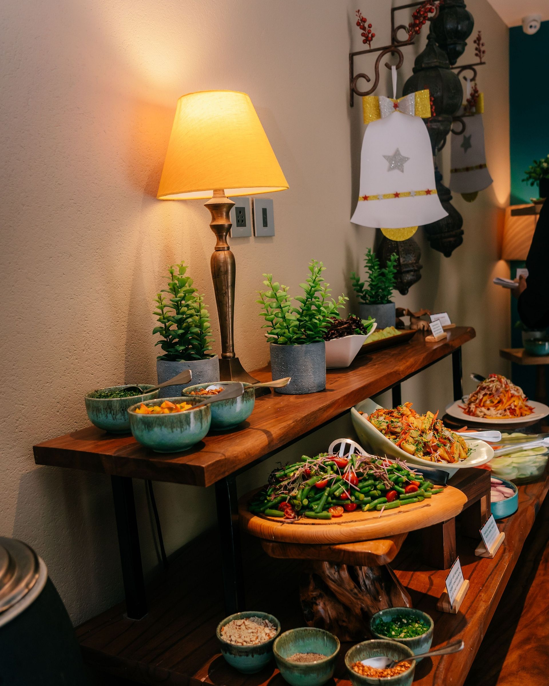 A cozy buffet setup with a variety of colorful salads, dips, and toppings, warmly lit by a lamp and decorated with potted plants and festive bells - Karma Chalets