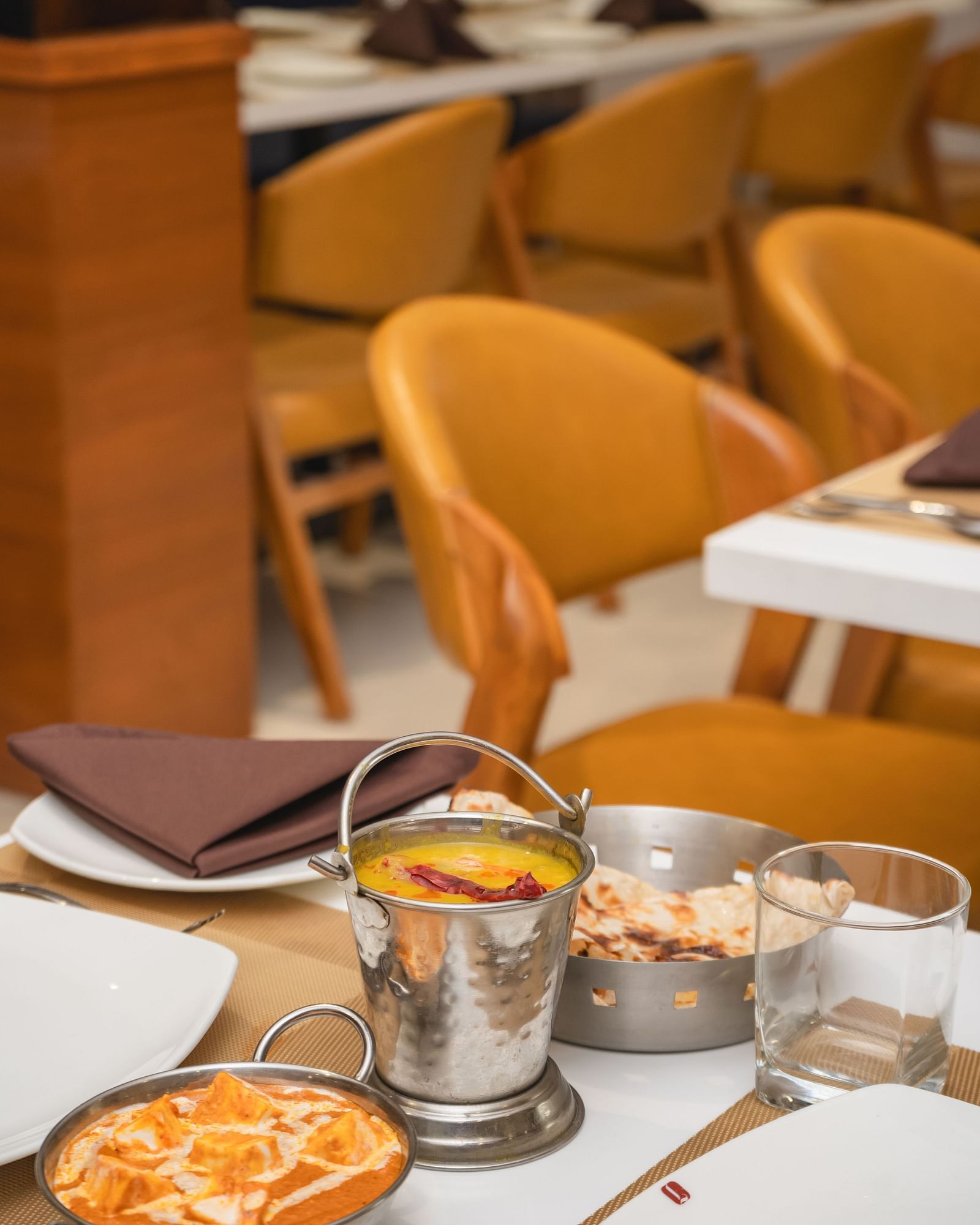 Bowls of food and drinks are arranged on a set table in a restaurant with empty chairs - Lords Eco Inn Ambaji.