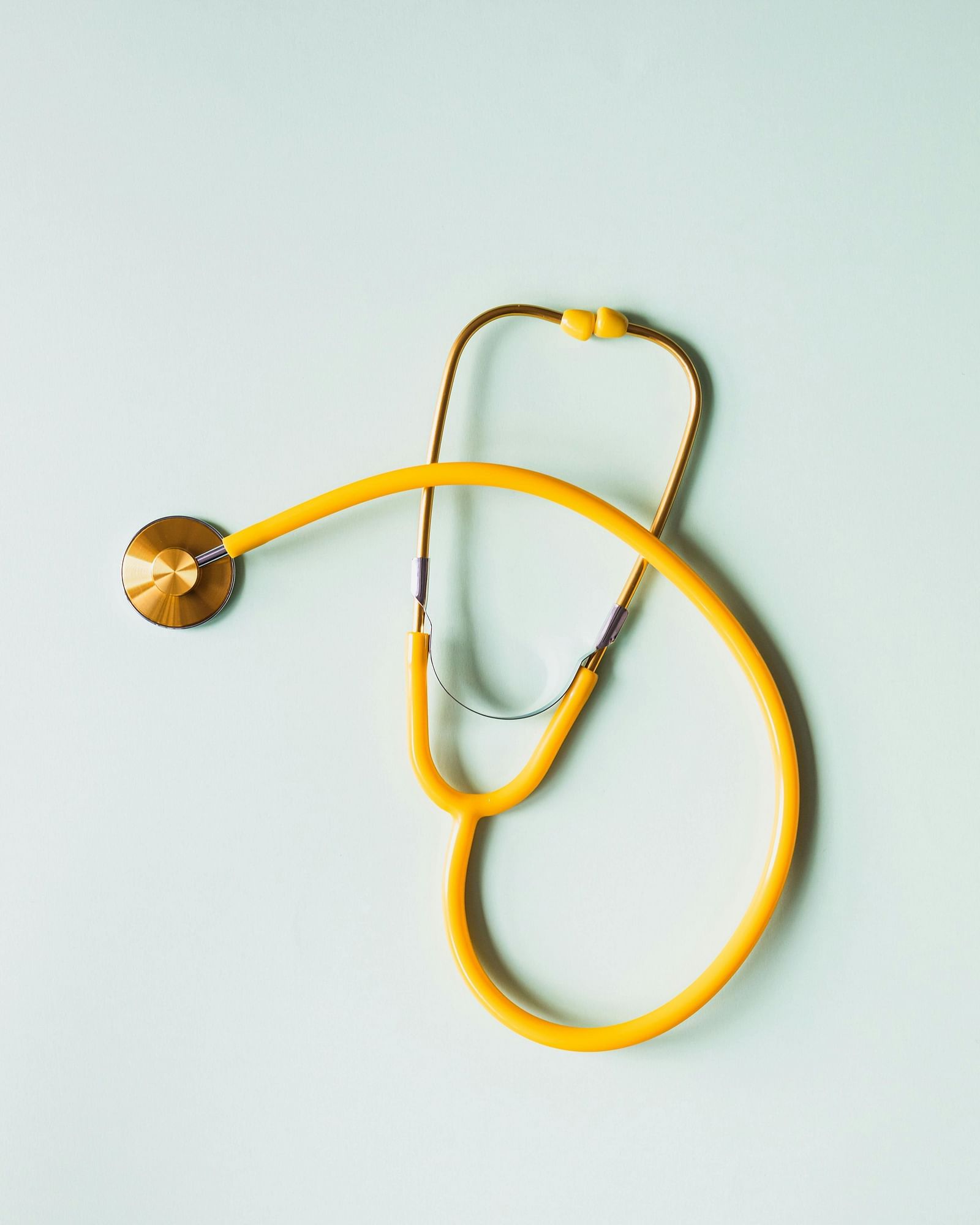 A golden stethoscope is hanging against a plain white background.