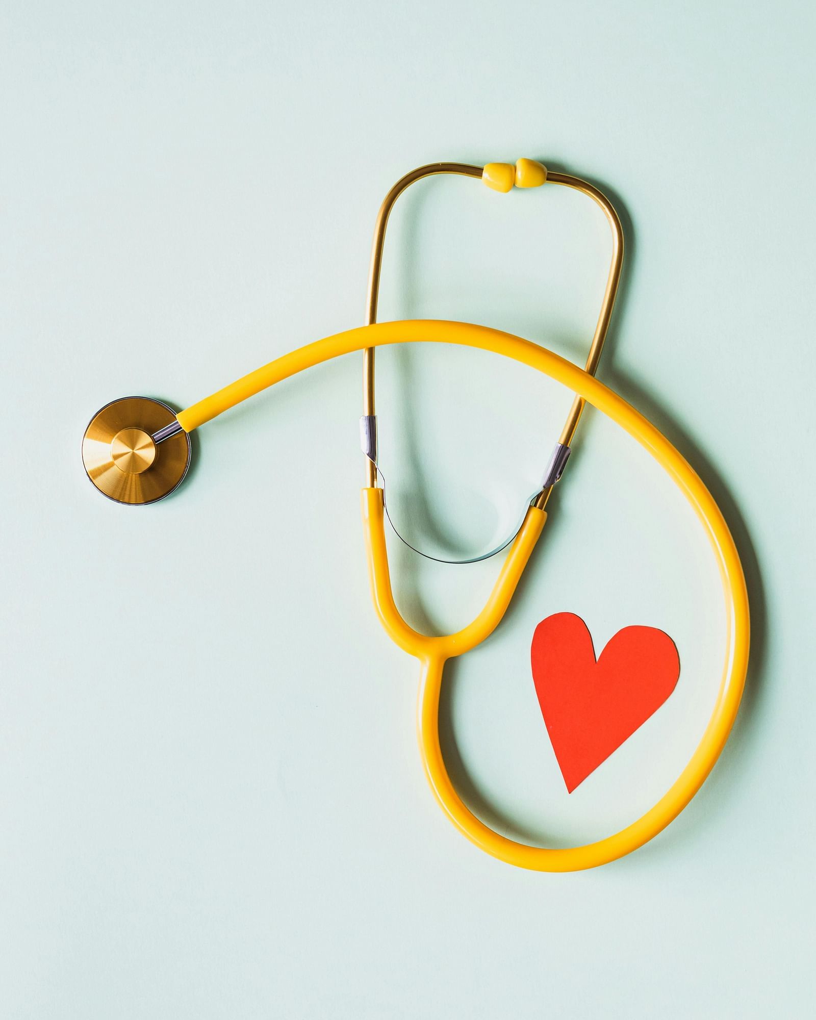 A yellow stethoscope forming a heart shape, with a small red heart symbol, against a white background.