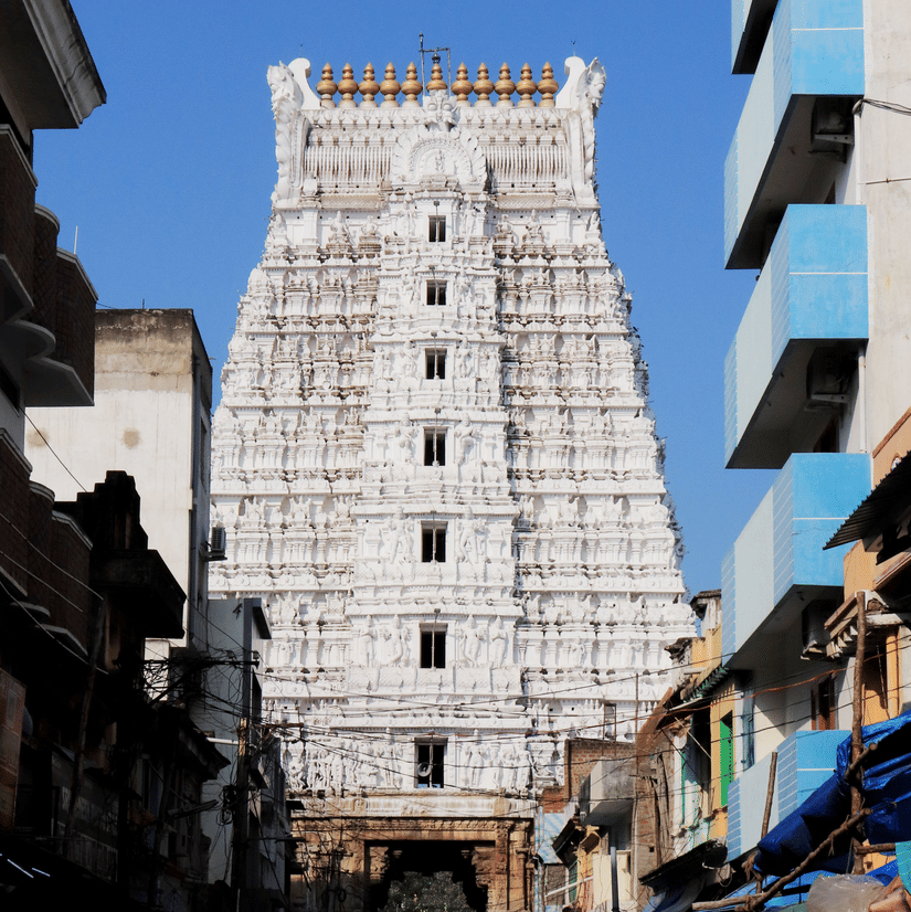 A view from afar of the majestic Govindaraja Temple in Tirupati, with people walking in front of it on the road.