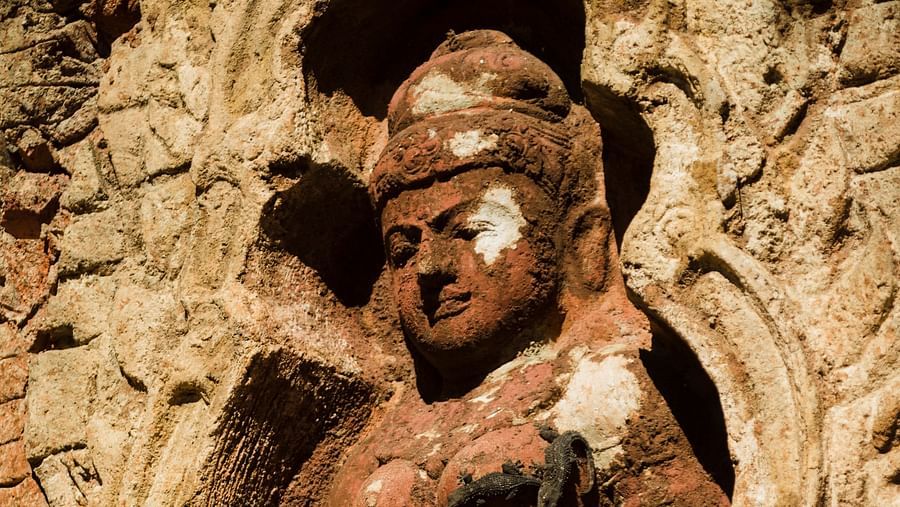 Terracotta sculpture of a female holding a vessel, set in an ancient wall.