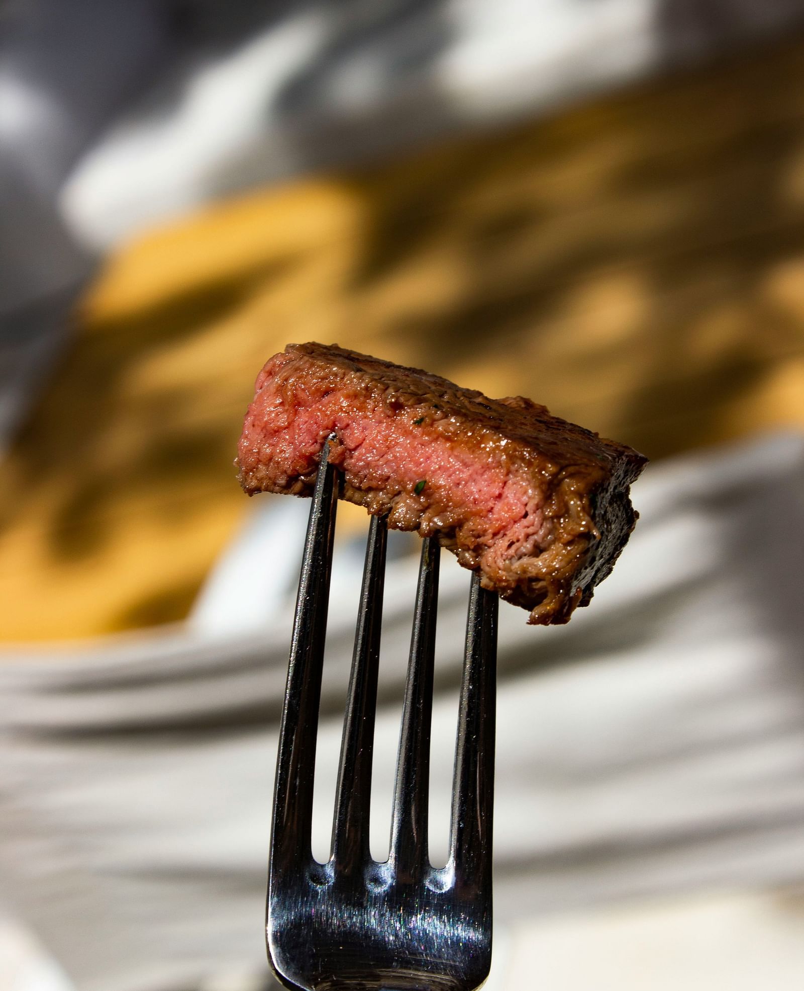 A slice of steak held up by a fork.