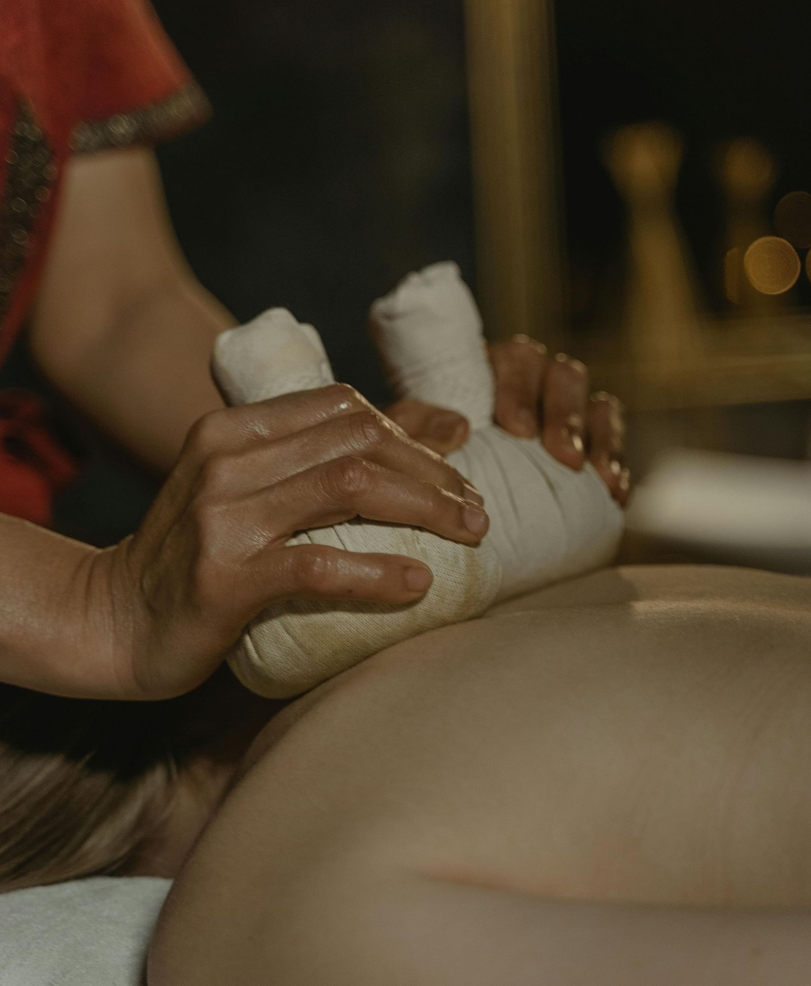 A masseuse using cloth bundles to press the back of a person.