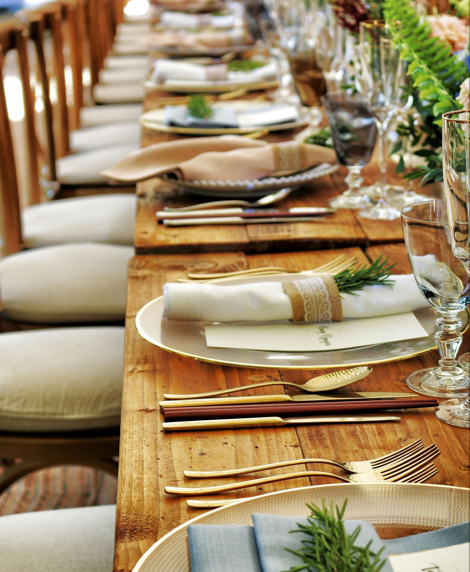 A long wooden table with beautifully set cutlery with small fern leaves in vases.