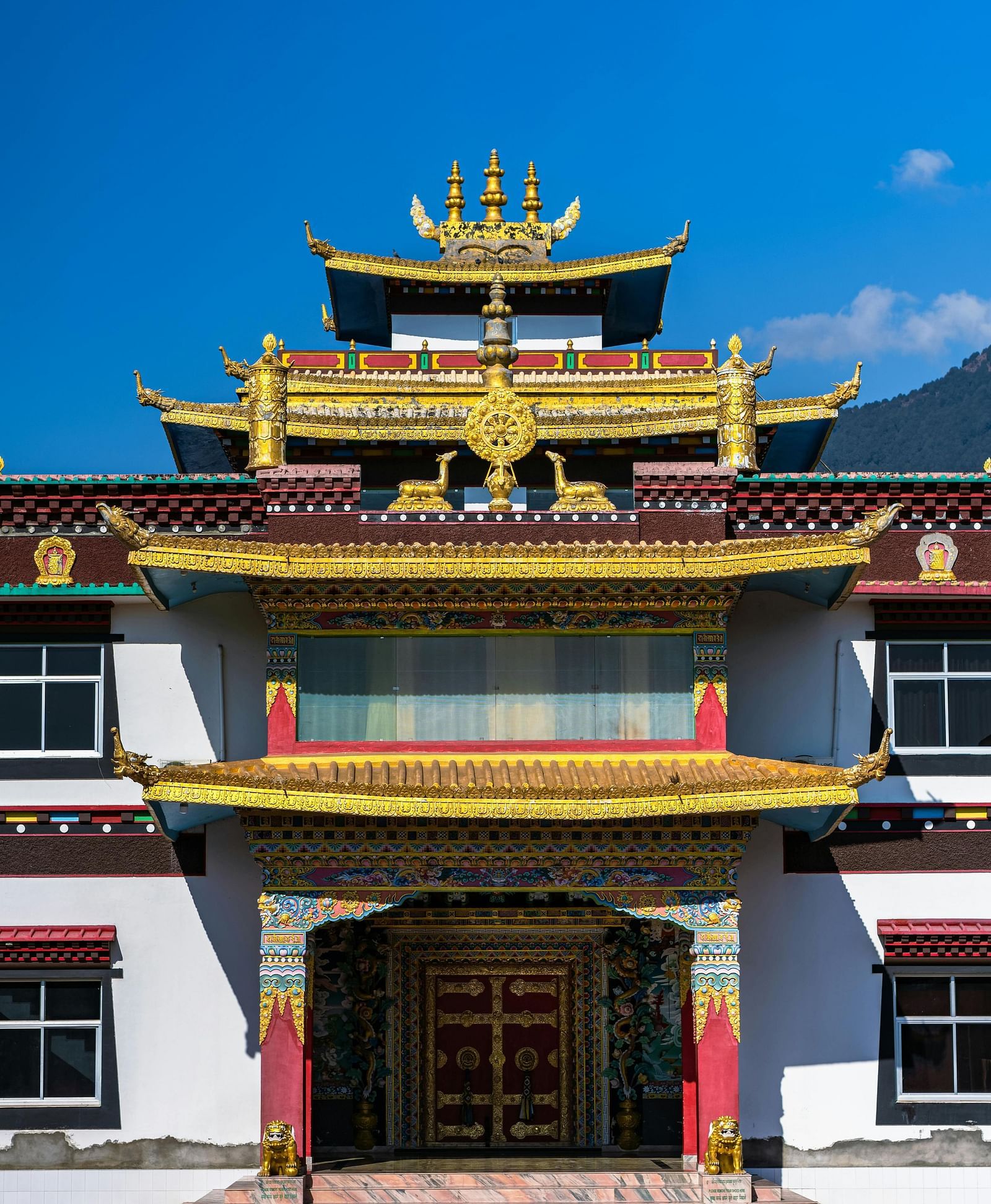 The vibrant front facade of a Tibetan monastery with elaborate golden decorations against a clear blue sky