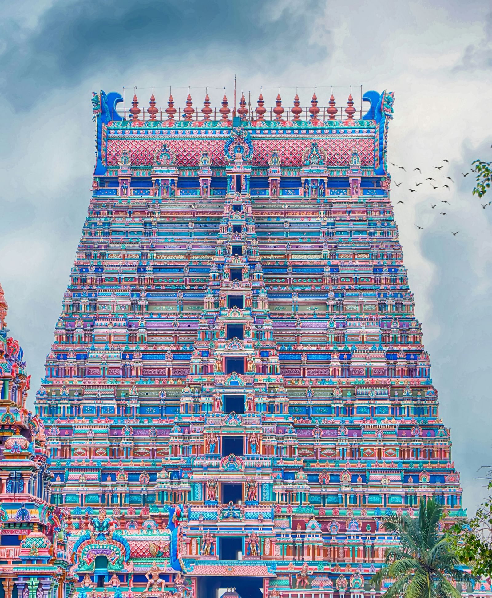 A vivid and intricately carved gopuram of a South Indian temple against a cloudy sky