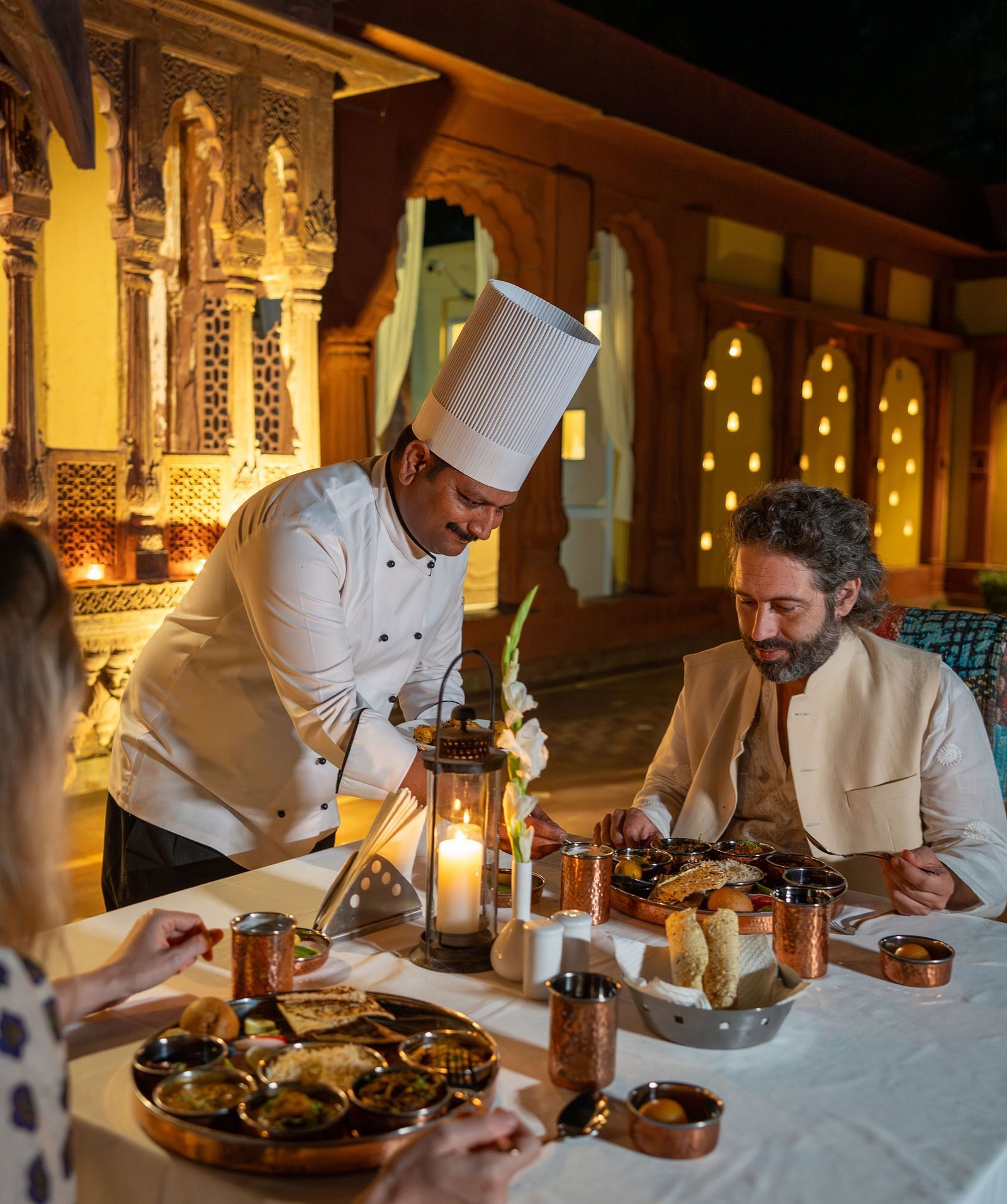 A chef serving two guests seated in a dining area at Surpura Bagh.