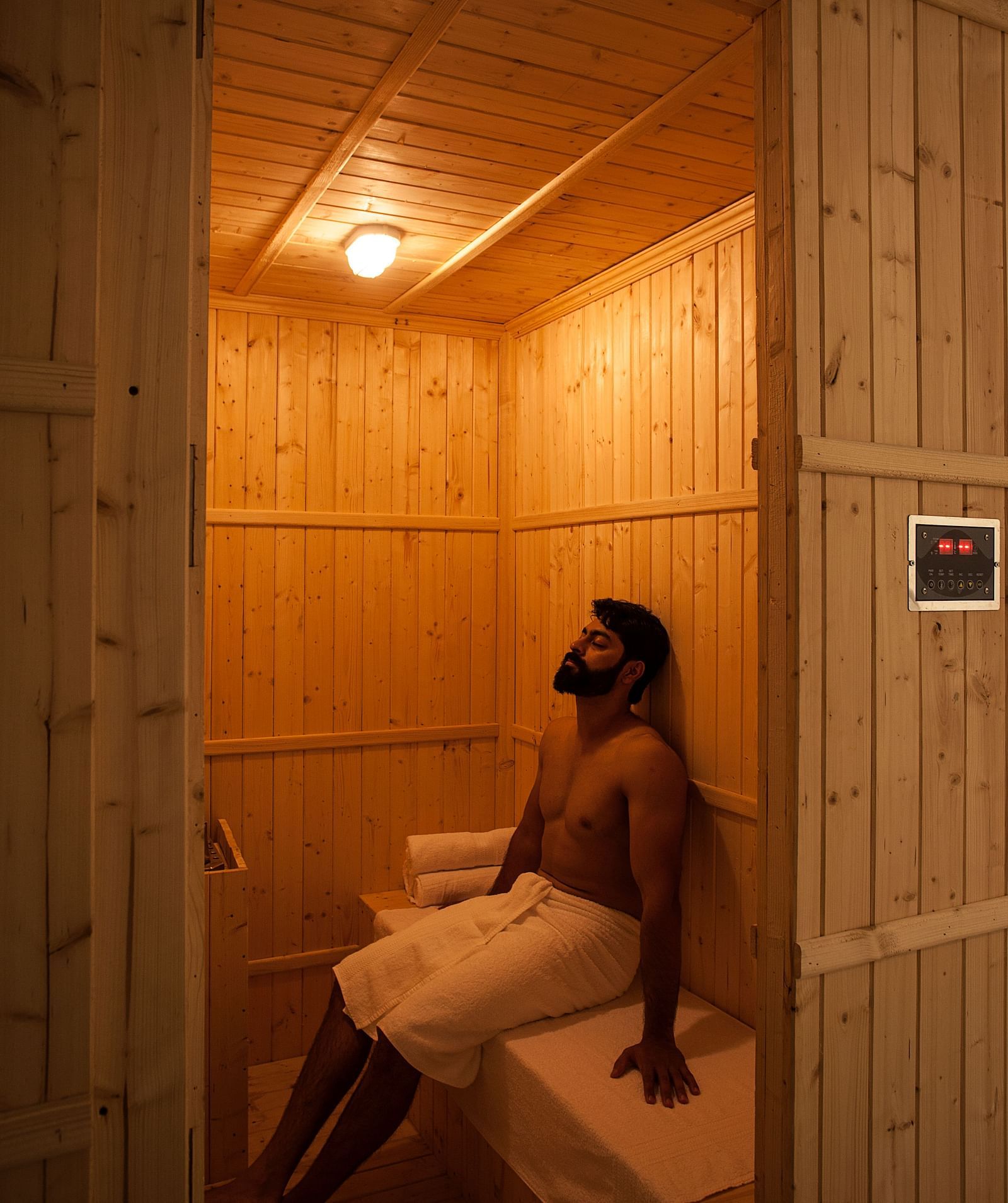 Person sitting in a wooden sauna, warm light, relaxation setting - Shreyas Retreat