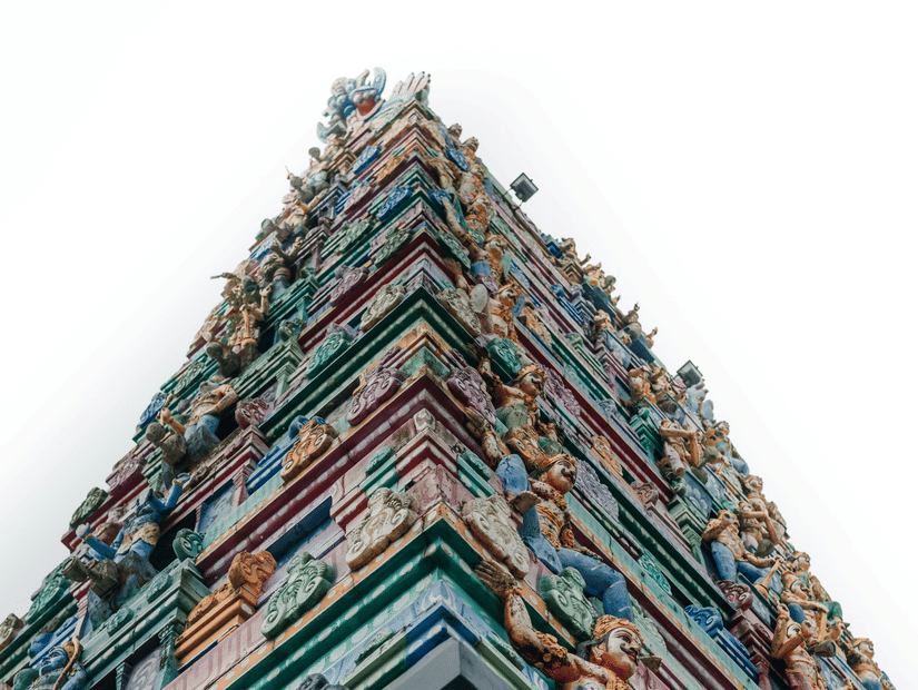 A view from below of a pillar holding the gopuram featuring numerous miniature deities on layered architecture.