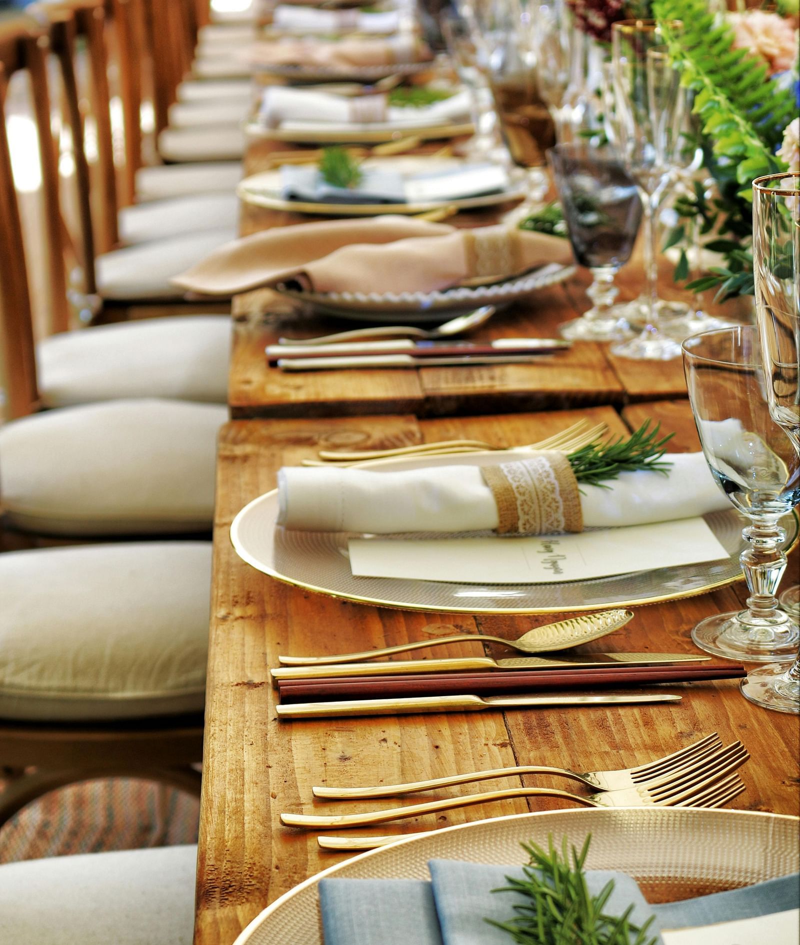 A long wooden table with beautifully set cutlery with small fern leaves in vases.