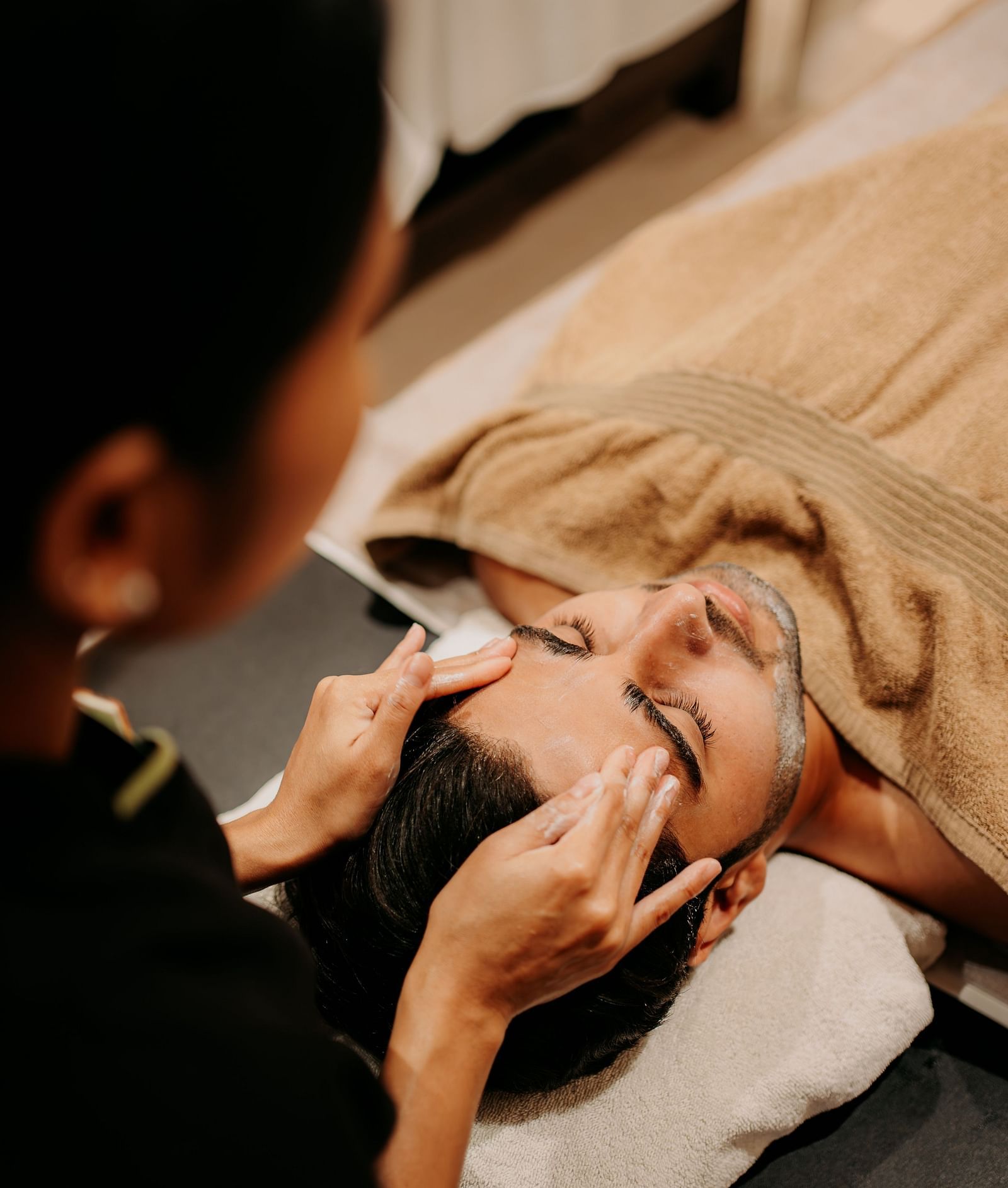 A spa staff member providing a head massage to a man relaxing on the bed at Crescent spa & resort, Indore