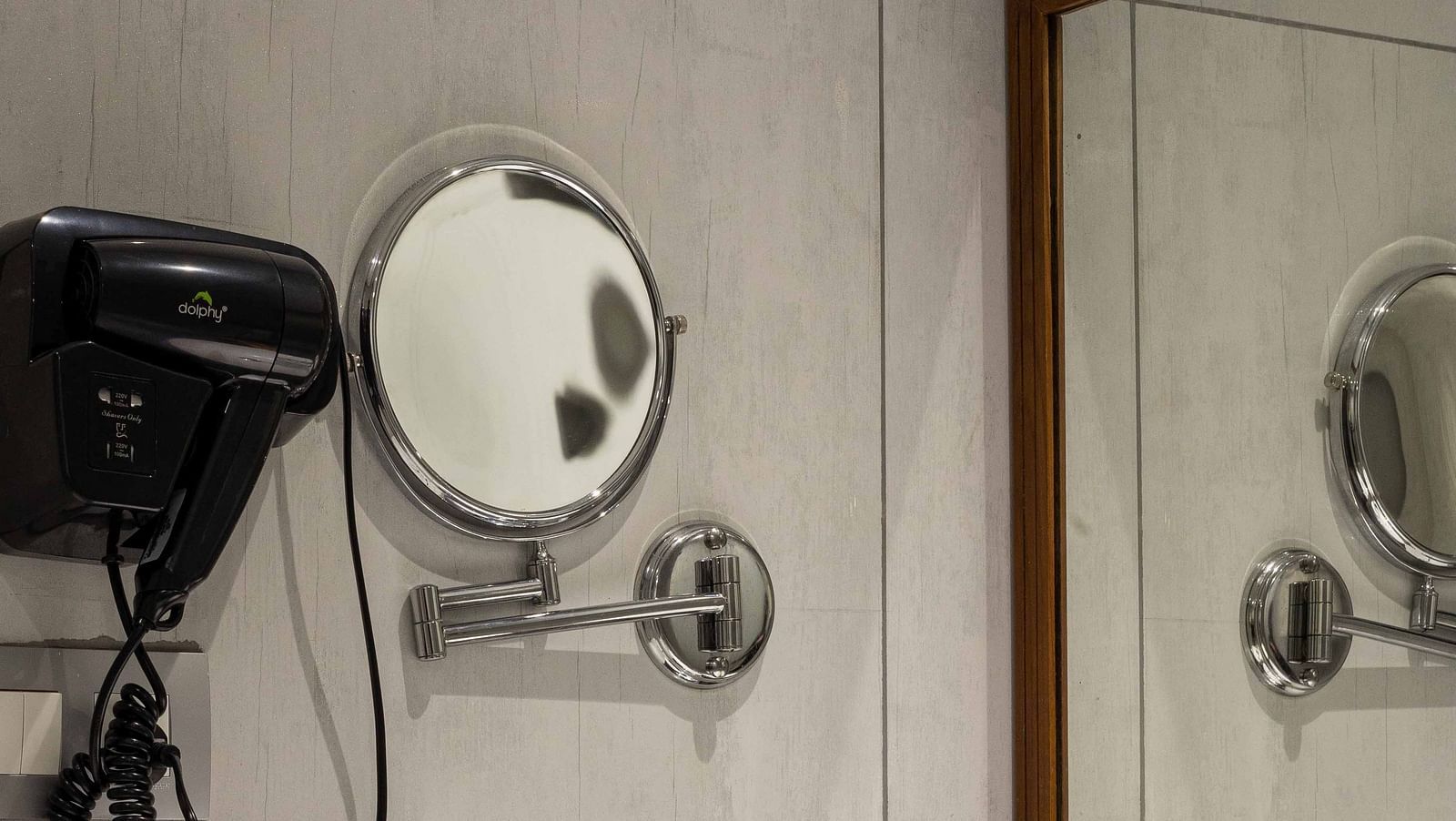 Image of the bathroom in Coral Premium Room at Coral Reef Hotel and Spa in Port Blair featuring a sink and a large mirror over it along with a hair dryer and mini shaving mirror next to it
