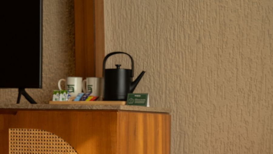 A cosy corner setup with a tea kettle, cups, and a chair beside a wooden cabinet at Ananta Spa and Resort, Ajabgarh.