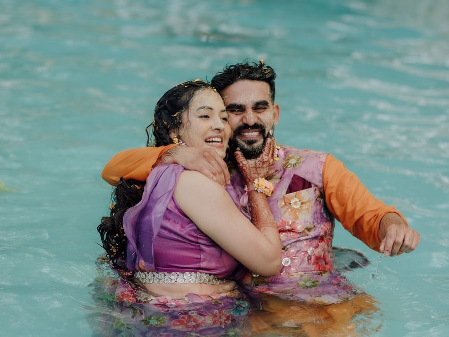 Bride and groom laughing while playing together in a swimming pool.