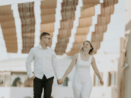 A view of a couple walking in Gewan Island, Qatar, holding hands with a makeshift roof in the background.