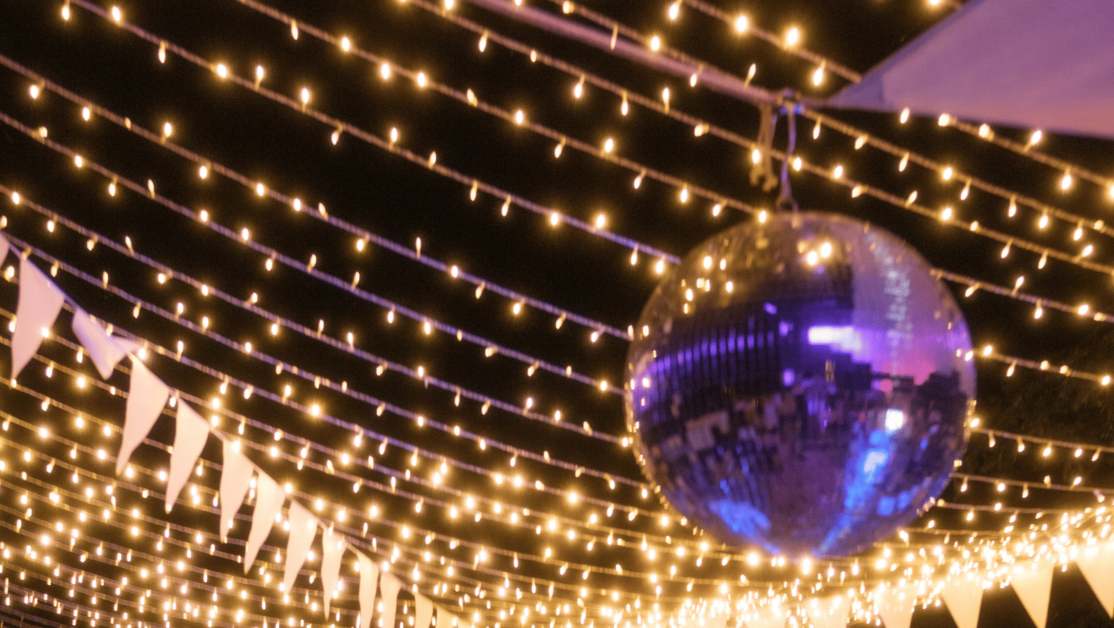 A view of a rooftop party with lights hung above and people dancing and talking to each other.