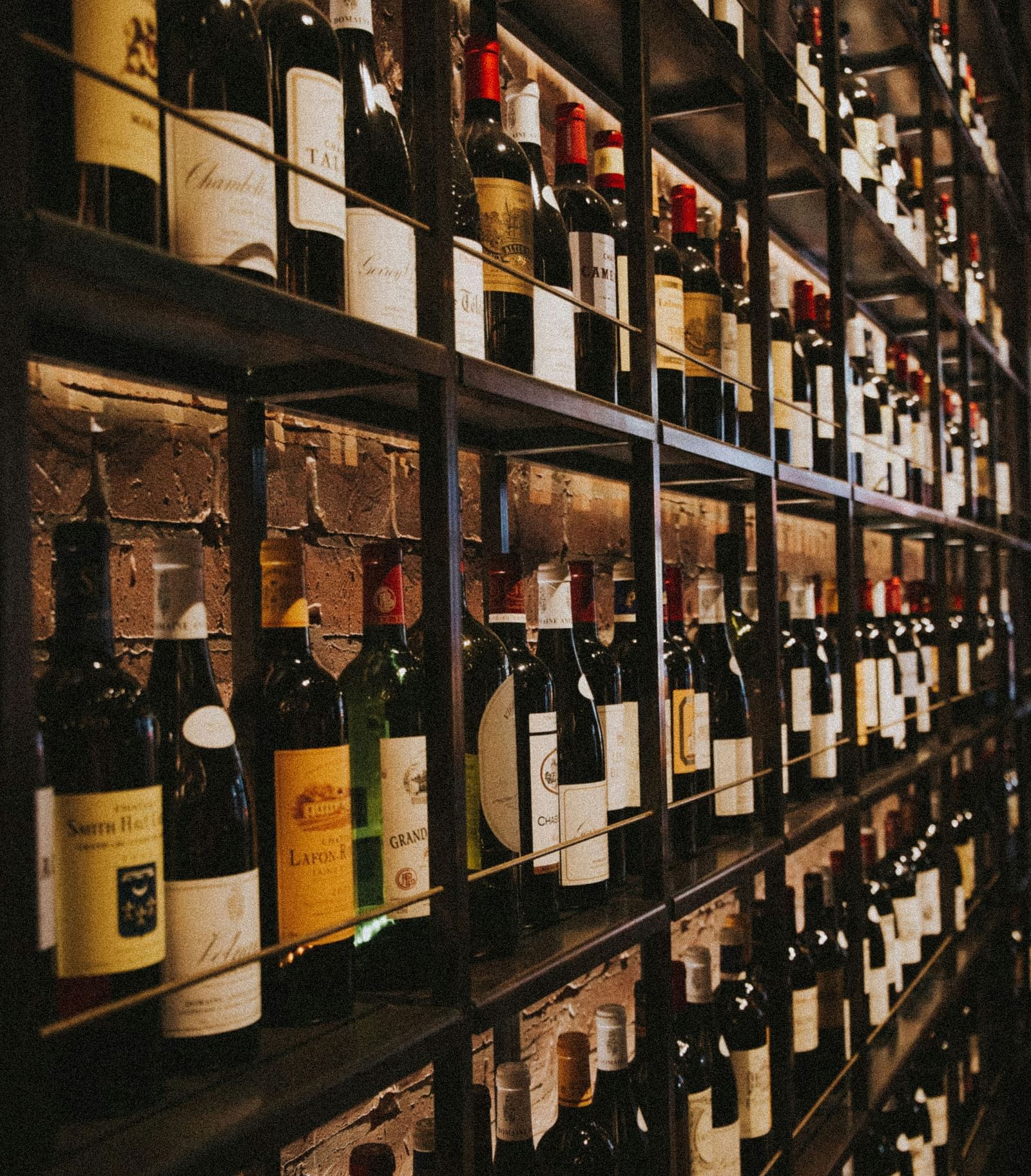 Shelves filled with a wide variety of wine bottles in a warmly lit cellar aisle.