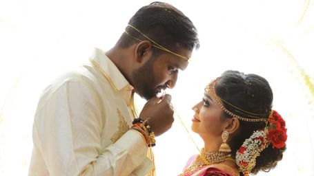 Bride and groom in traditional attire sharing a tender moment during a wedding ceremony, standing close and smiling.