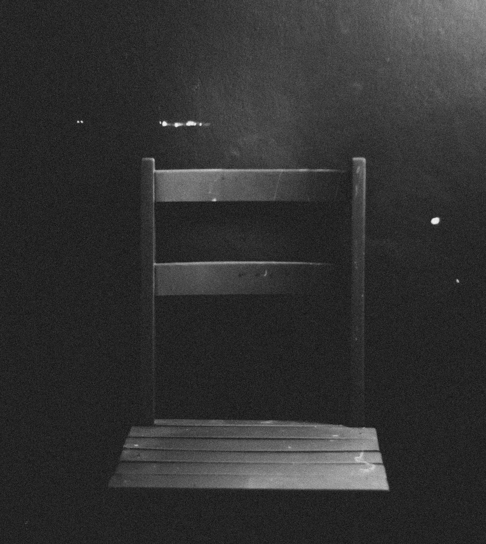 Black and white image of an empty chair against a dark backdrop.